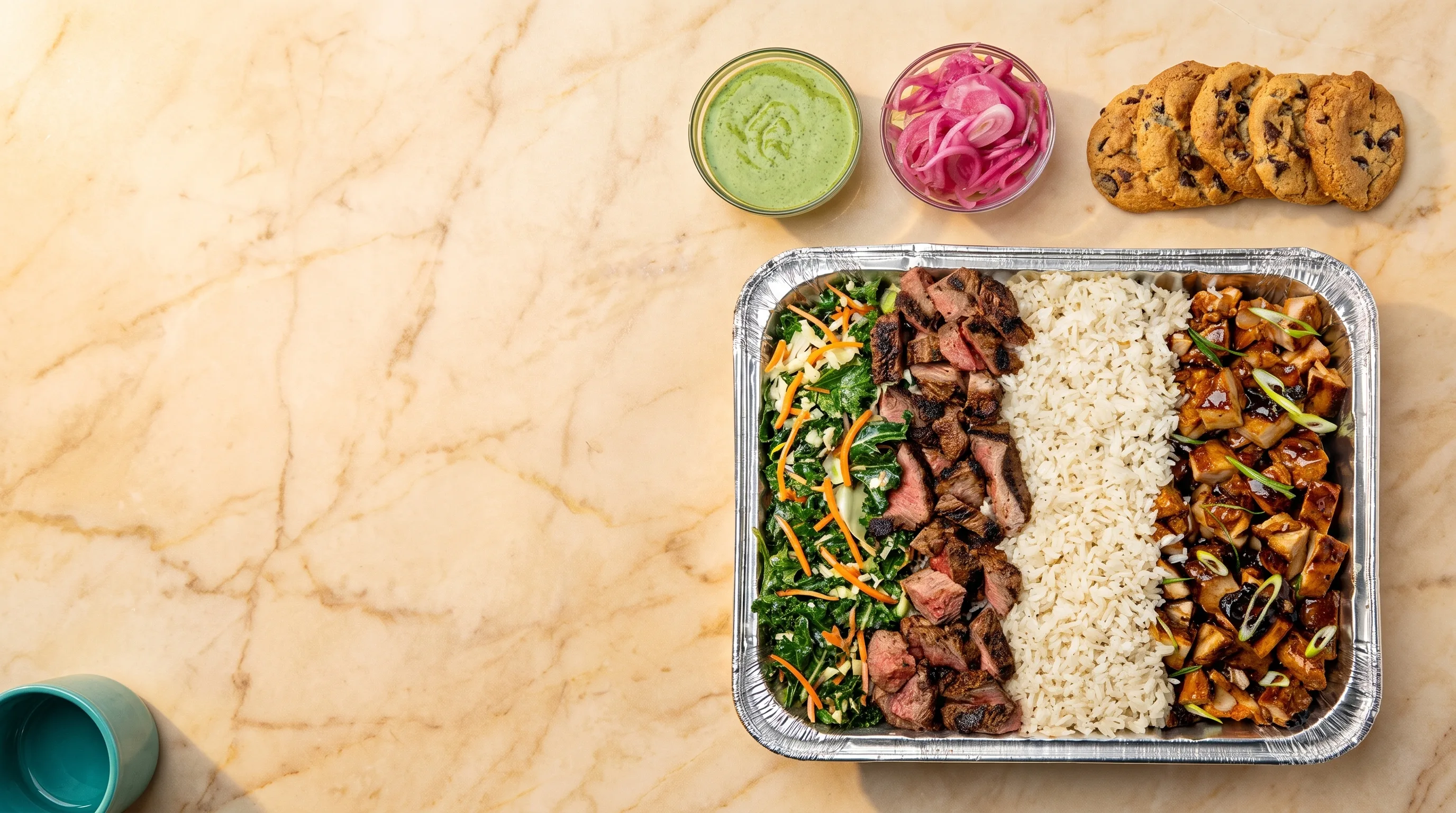 A Bolay catering spread with steak, chicken, rice, kale slaw, signature sauces and cookies